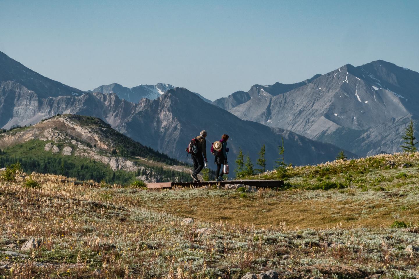 Hikers walking on a mountain trail with rugged peaks in the background.