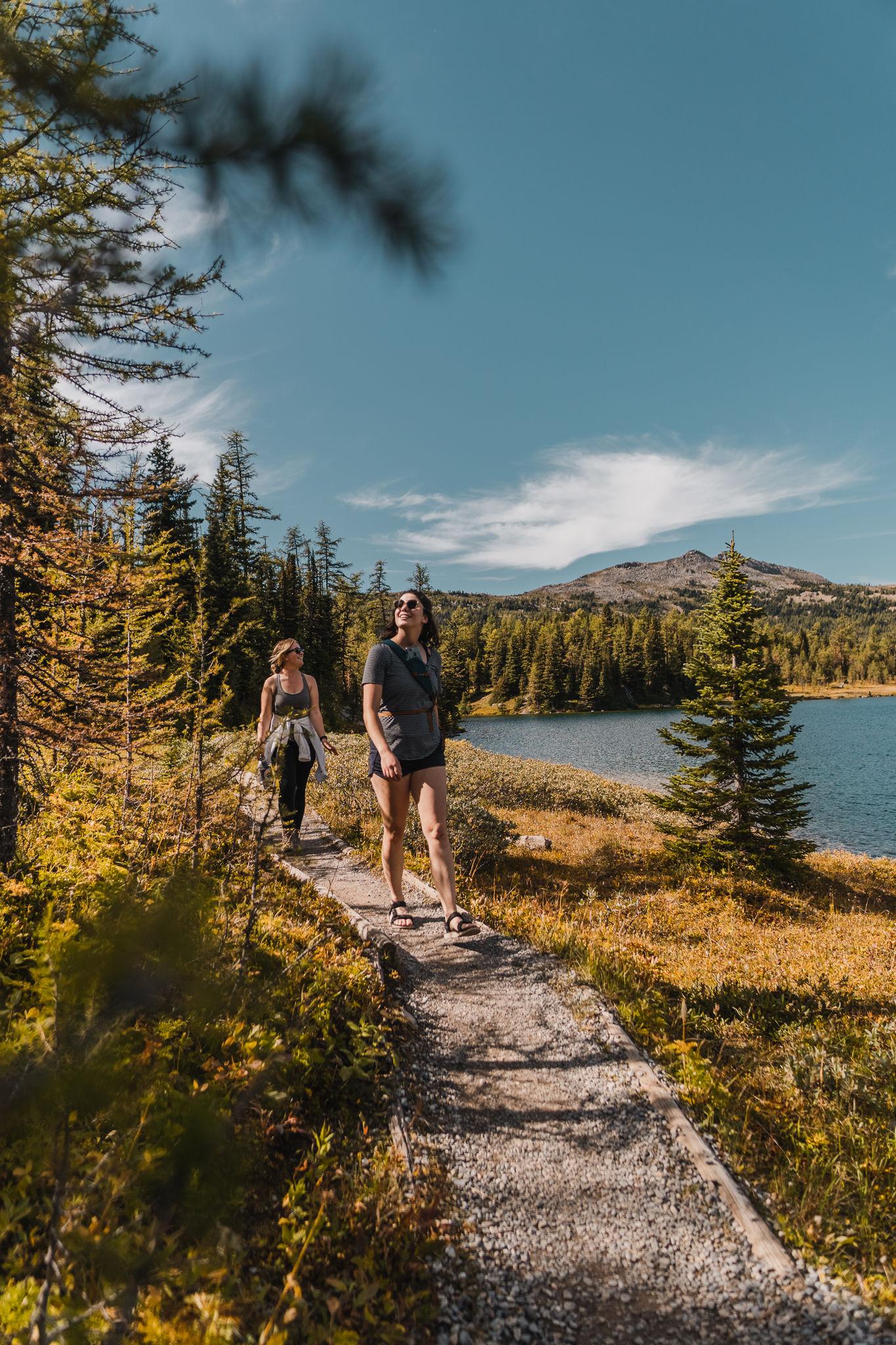 Two people hiking on a scenic trail by a lake, clear sky above.