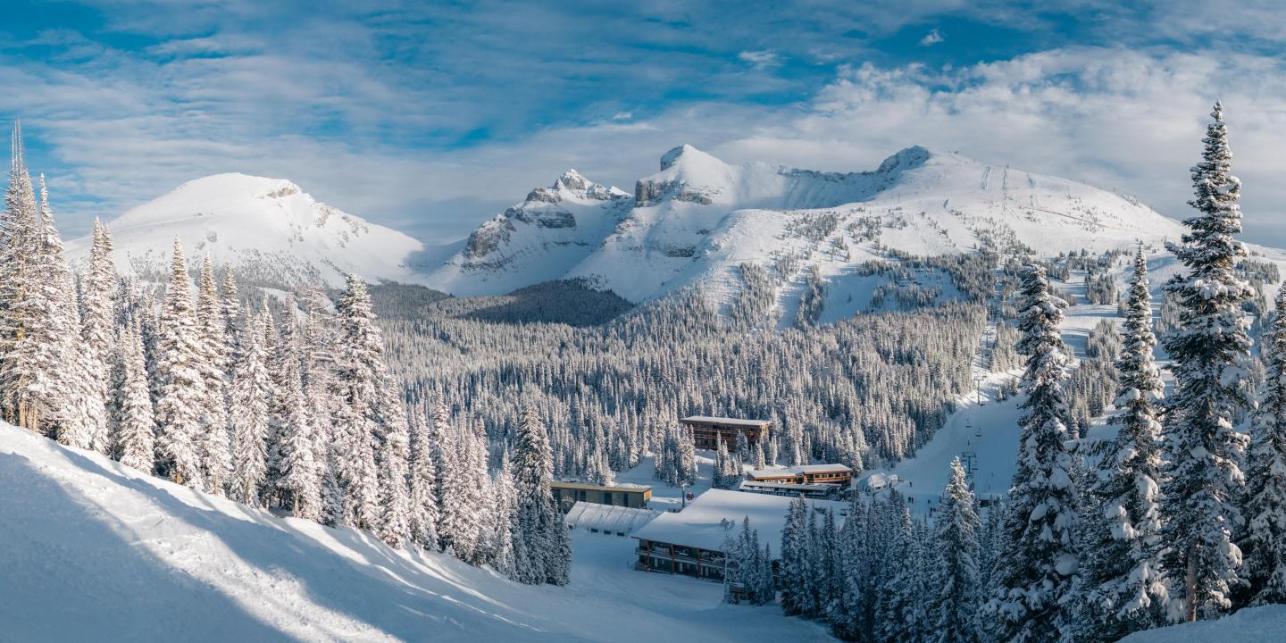 Snowy mountain landscape with evergreen trees and a ski resort below.
