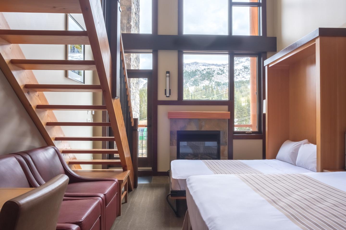 Cozy hotel room with two beds, a fireplace, and a large window view of mountains.
