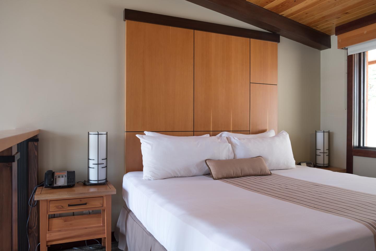 Cozy bedroom with wooden accents, neatly made bed, and bedside lamps.