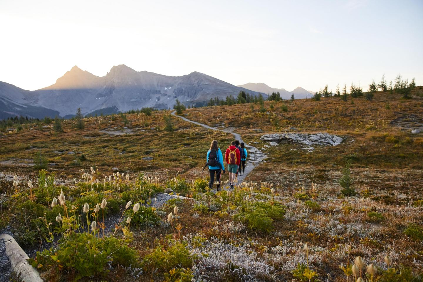 Hikers on a trail in a mountain landscape at sunset.