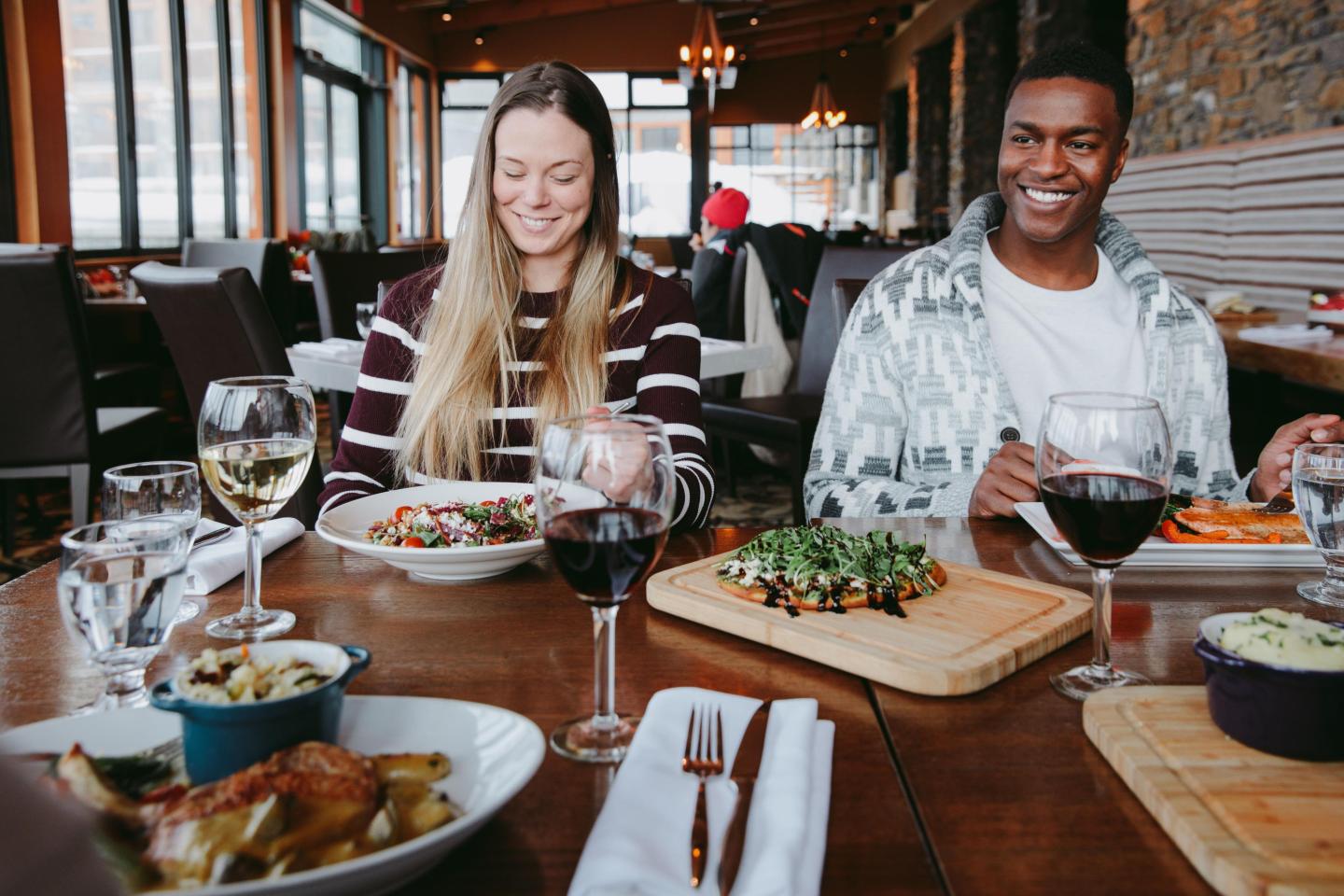 Friends enjoying a meal at a restaurant, with dishes and glasses of wine on the table.
