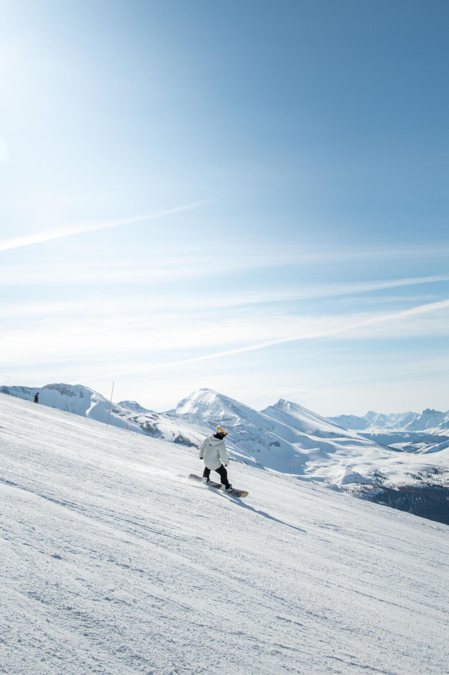 Skier descending snowy mountain under clear blue sky.