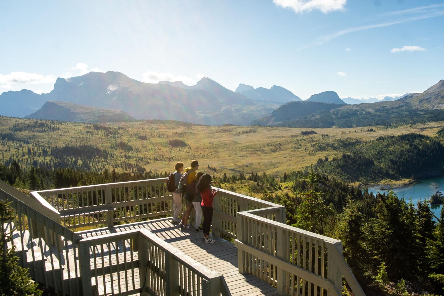 People on a wooden deck overlooking a scenic mountain landscape.