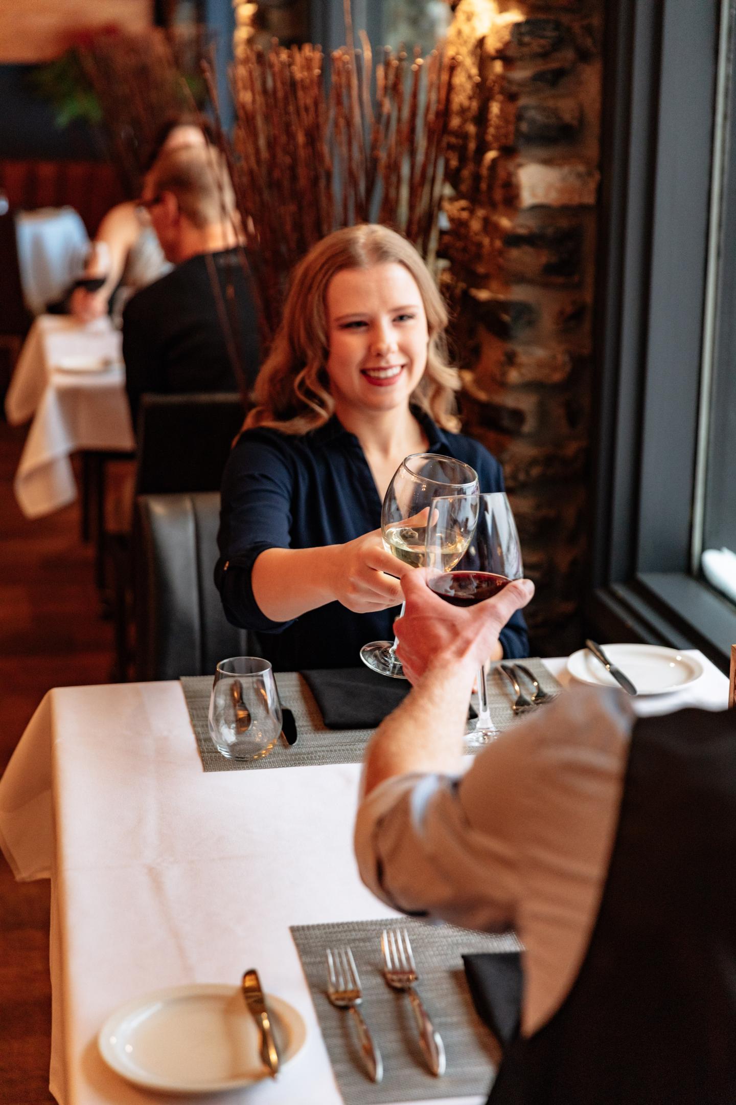 Dining couple clinking glasses, smiling in a cozy restaurant.