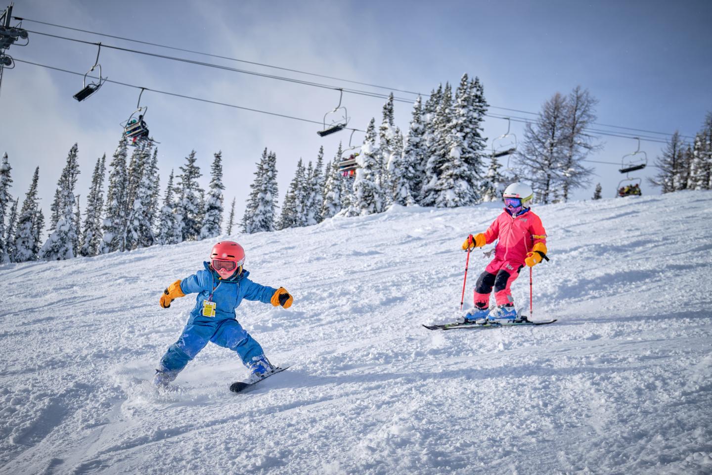Child and adult skiing on snowy slope under cloudy sky.