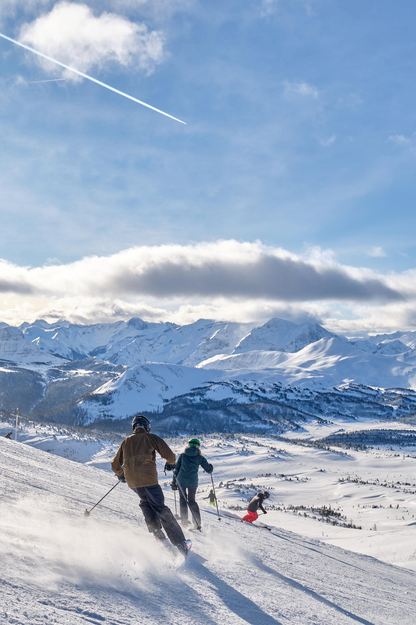 Skiers descending a snowy mountain under a clear blue sky.