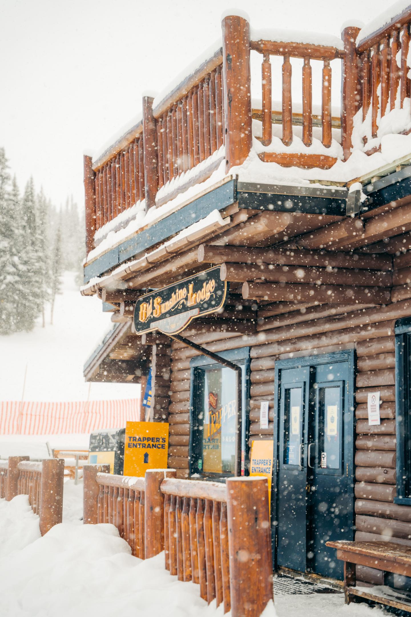 Snow-covered log cabin with a wooden balcony in a snowy landscape.