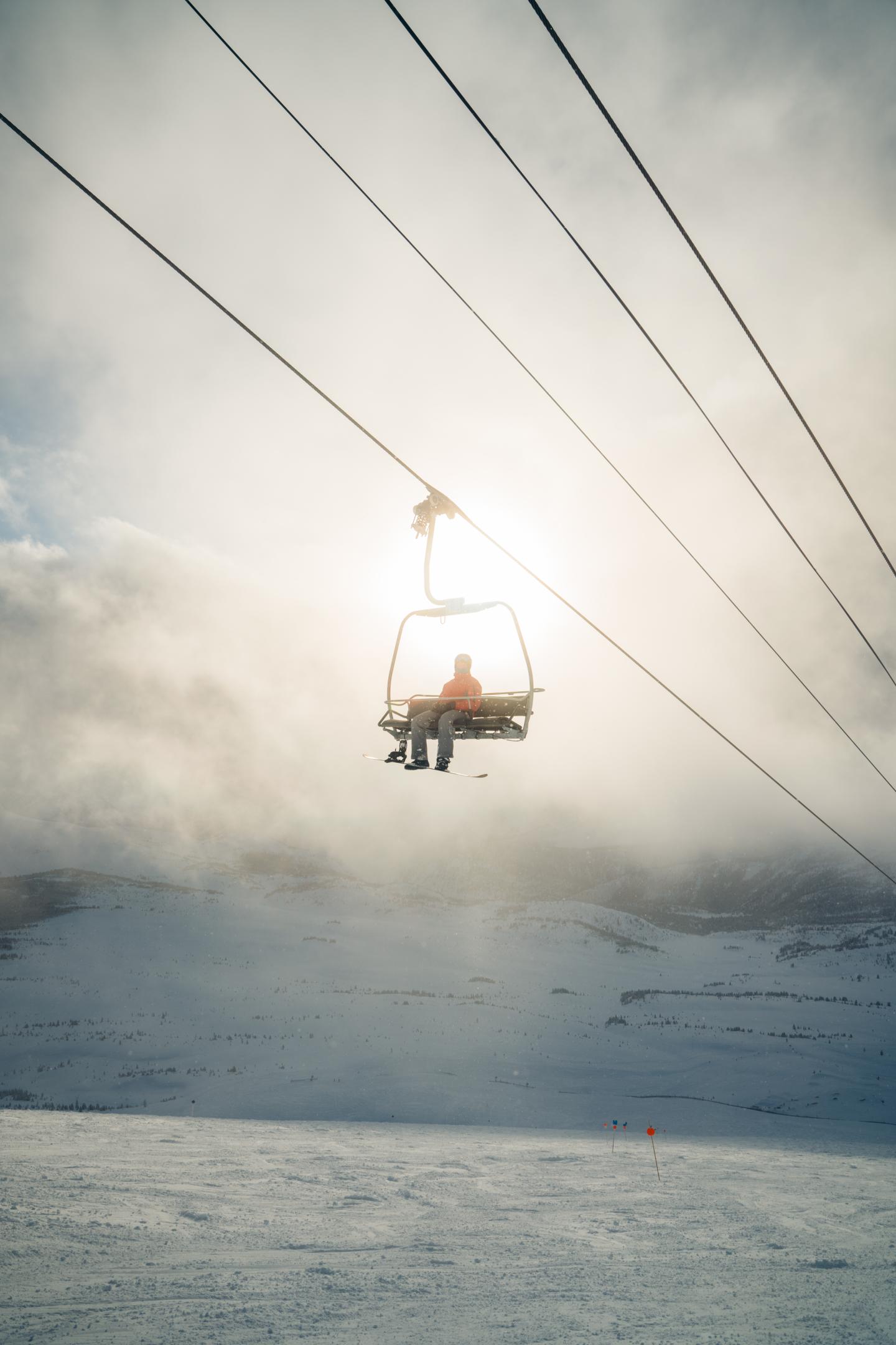 Person suspended in a chair beneath power lines over a cloudy ocean.