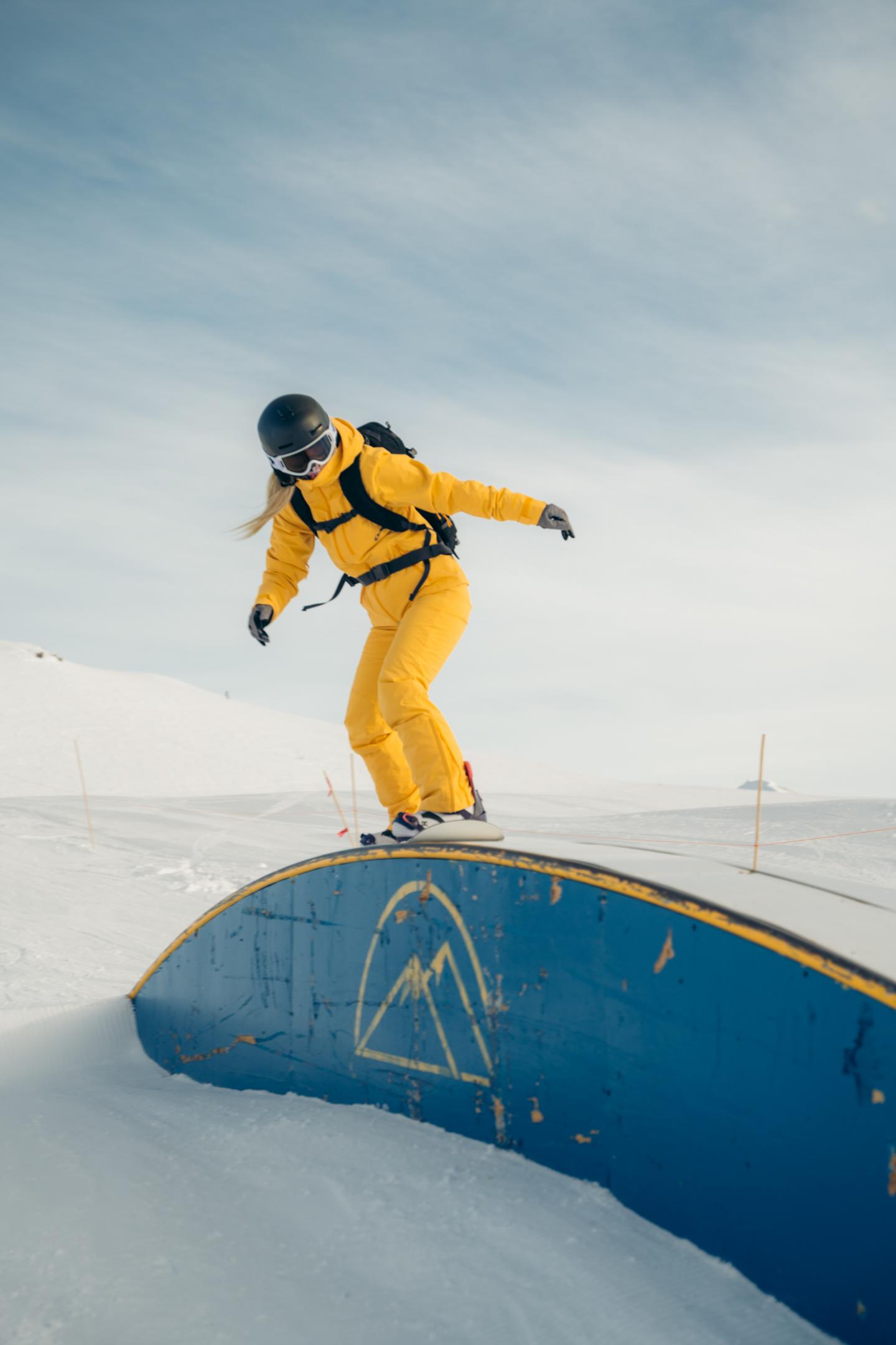 Snowboarder in yellow outfit grinding a blue rail at a snowy park.