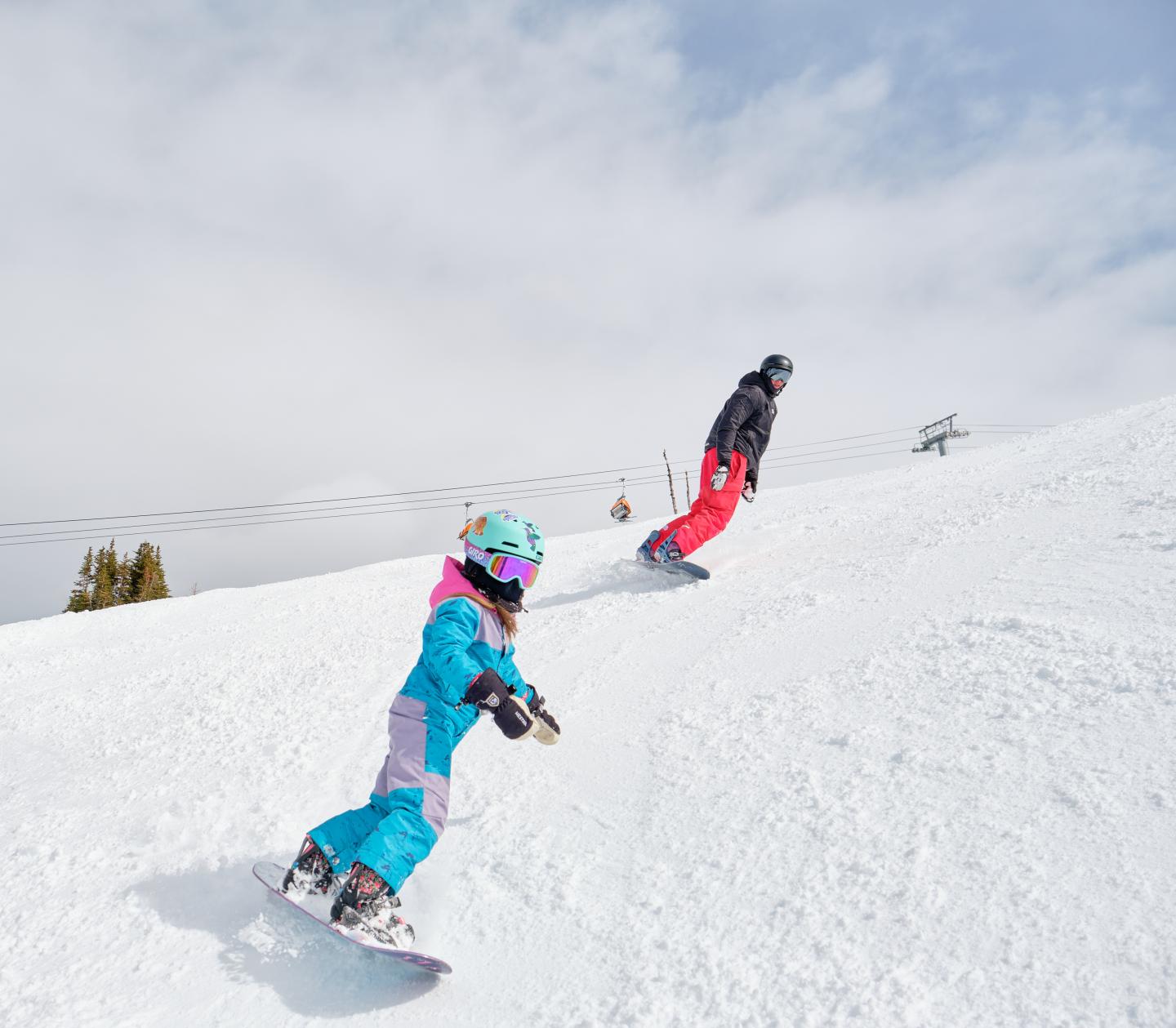 Two snowboarders descending a snowy slope under a cloudy sky.