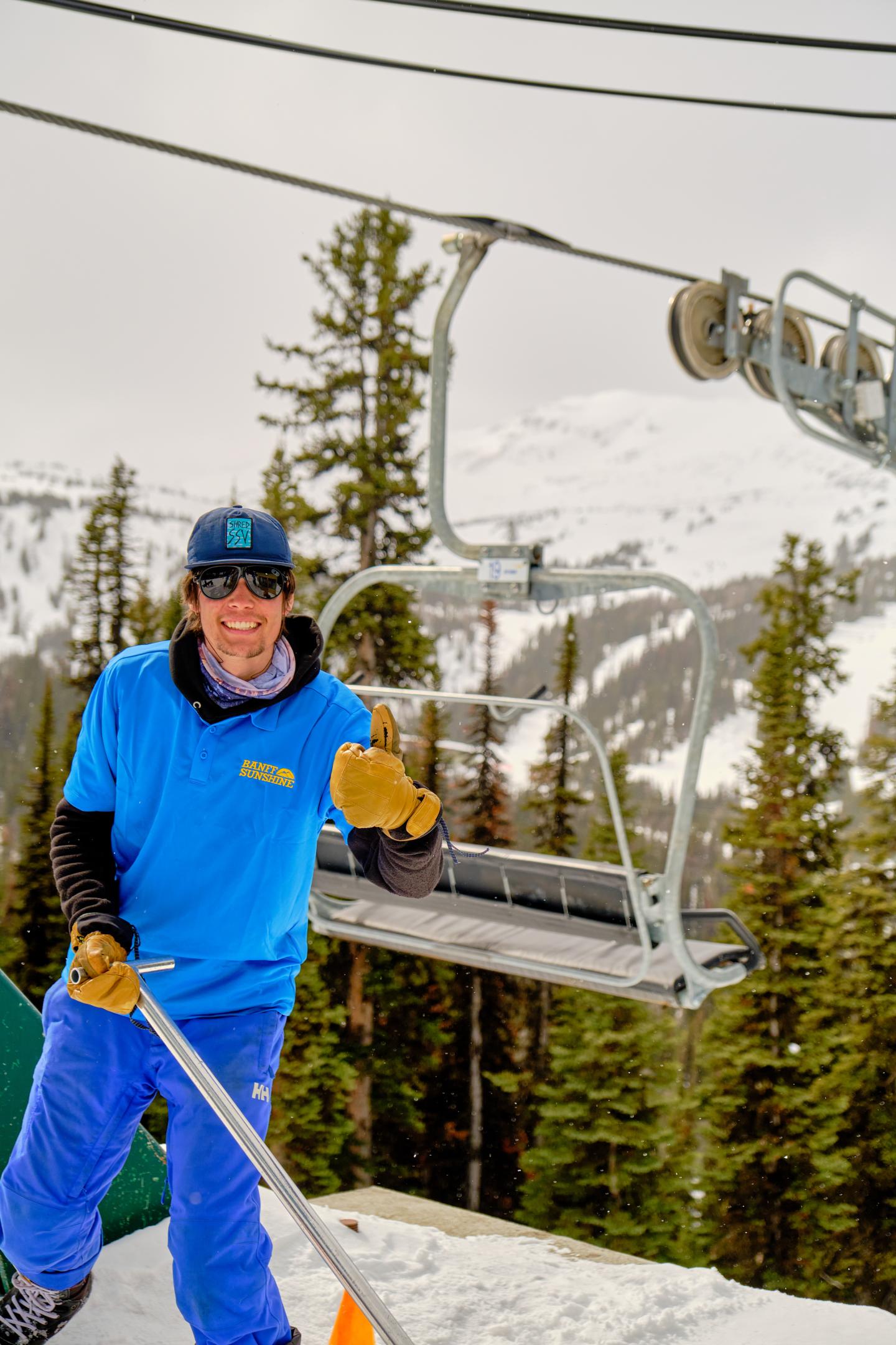 Ski patroller in blue uniform beside an empty chairlift on a snowy slope.