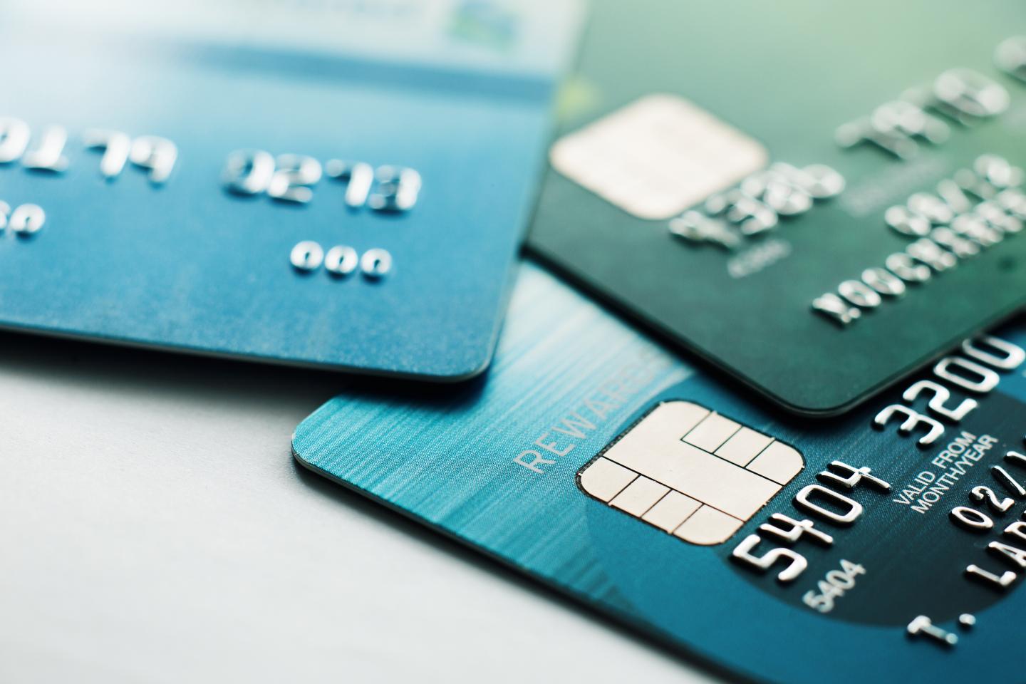 Three stacked credit cards in blue and green shades on a light surface.