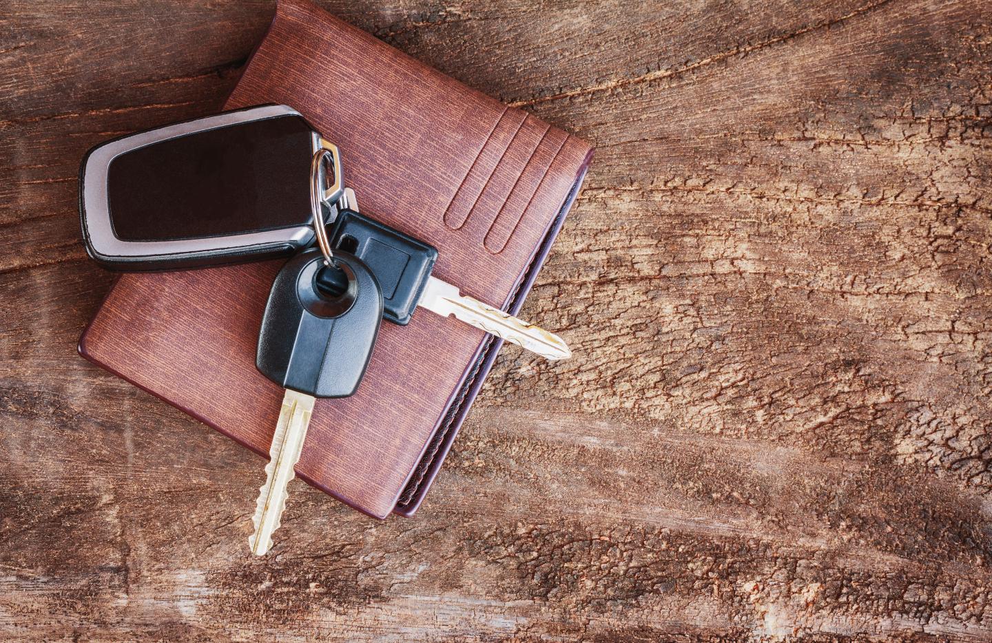 Car keys on a brown wallet on wooden surface.