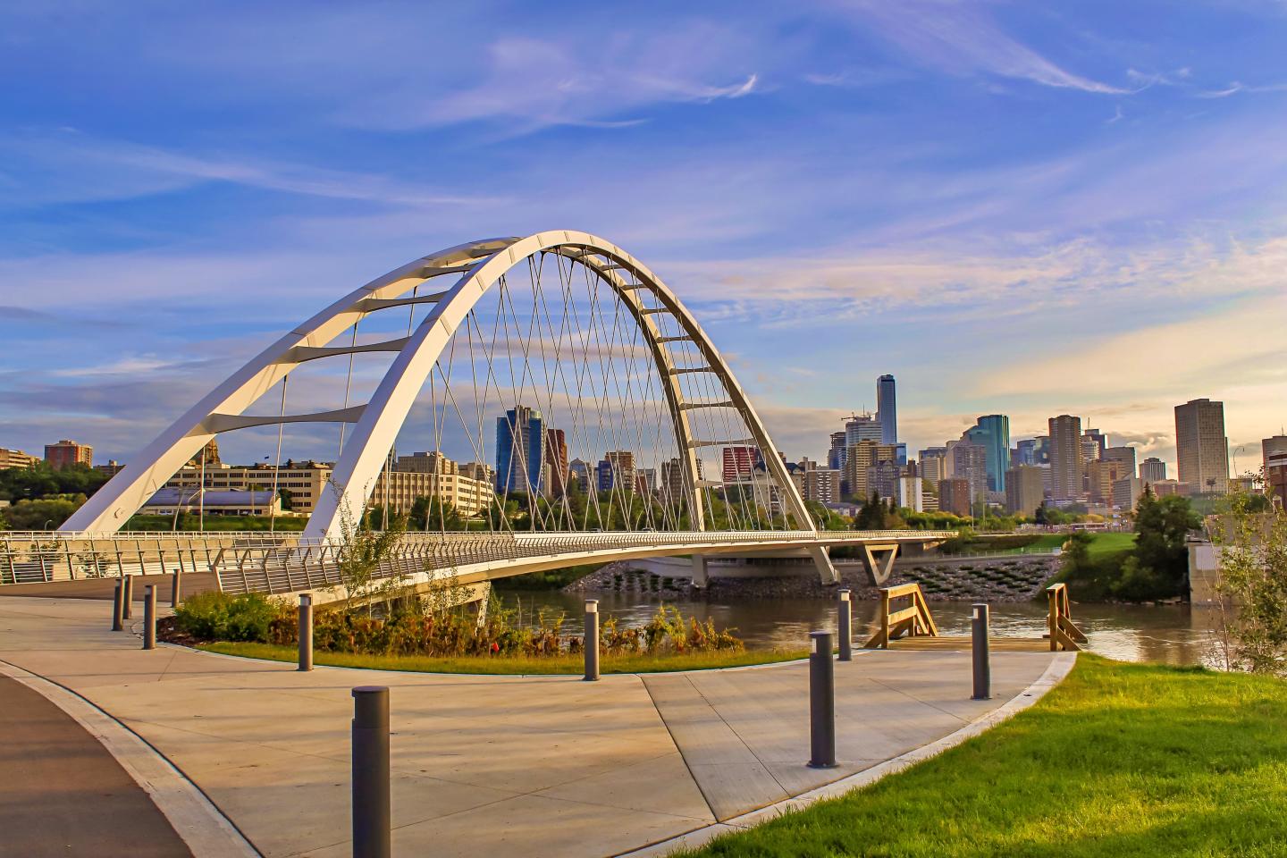 Arched bridge over a river with a city skyline under a vibrant blue sky.