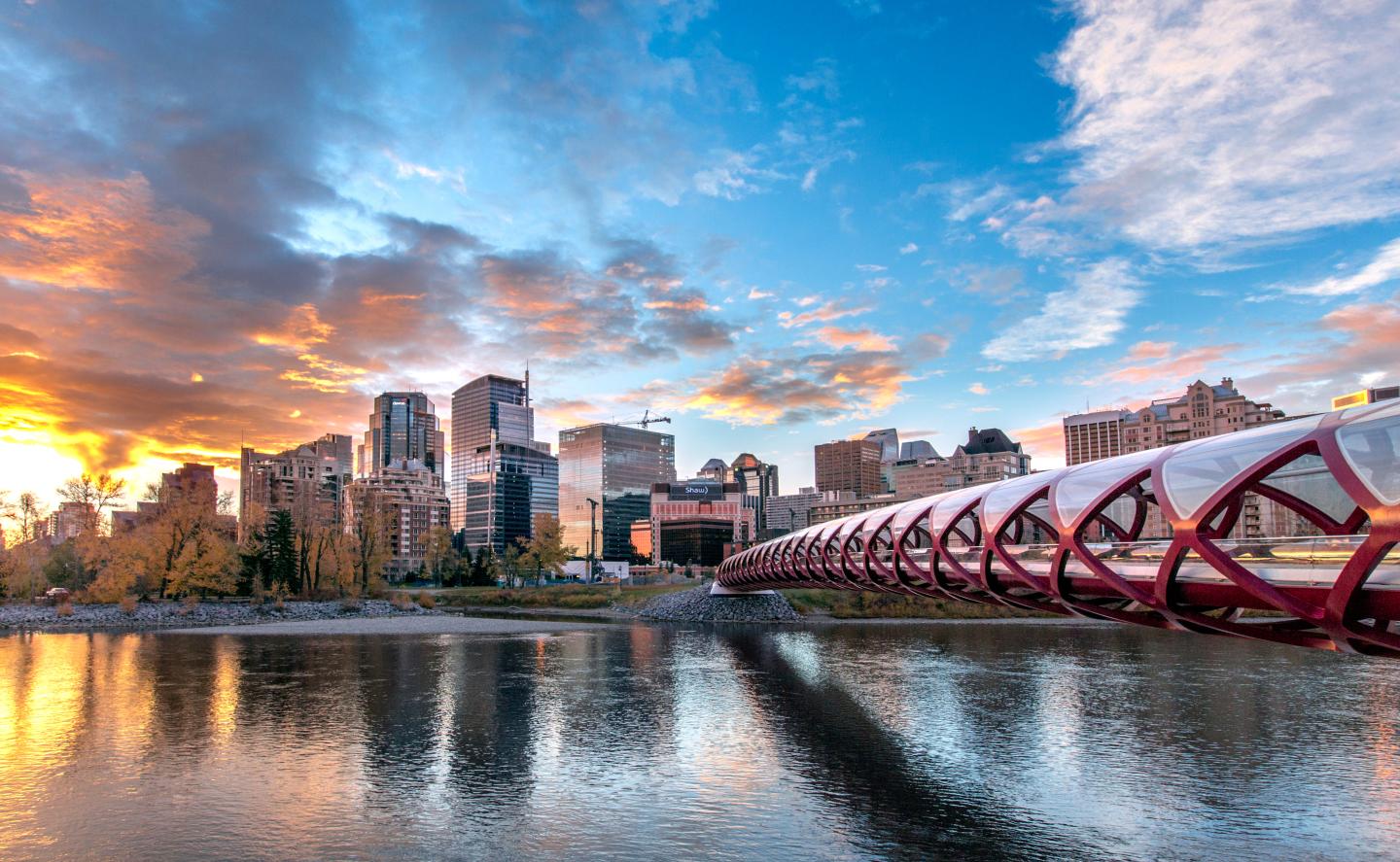 Skyline with a red bridge over a calm river at sunset.