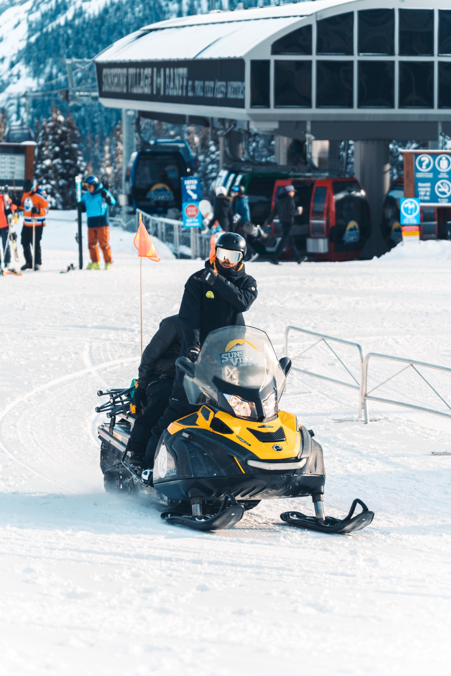 Person riding a yellow snowmobile in a snowy ski area.