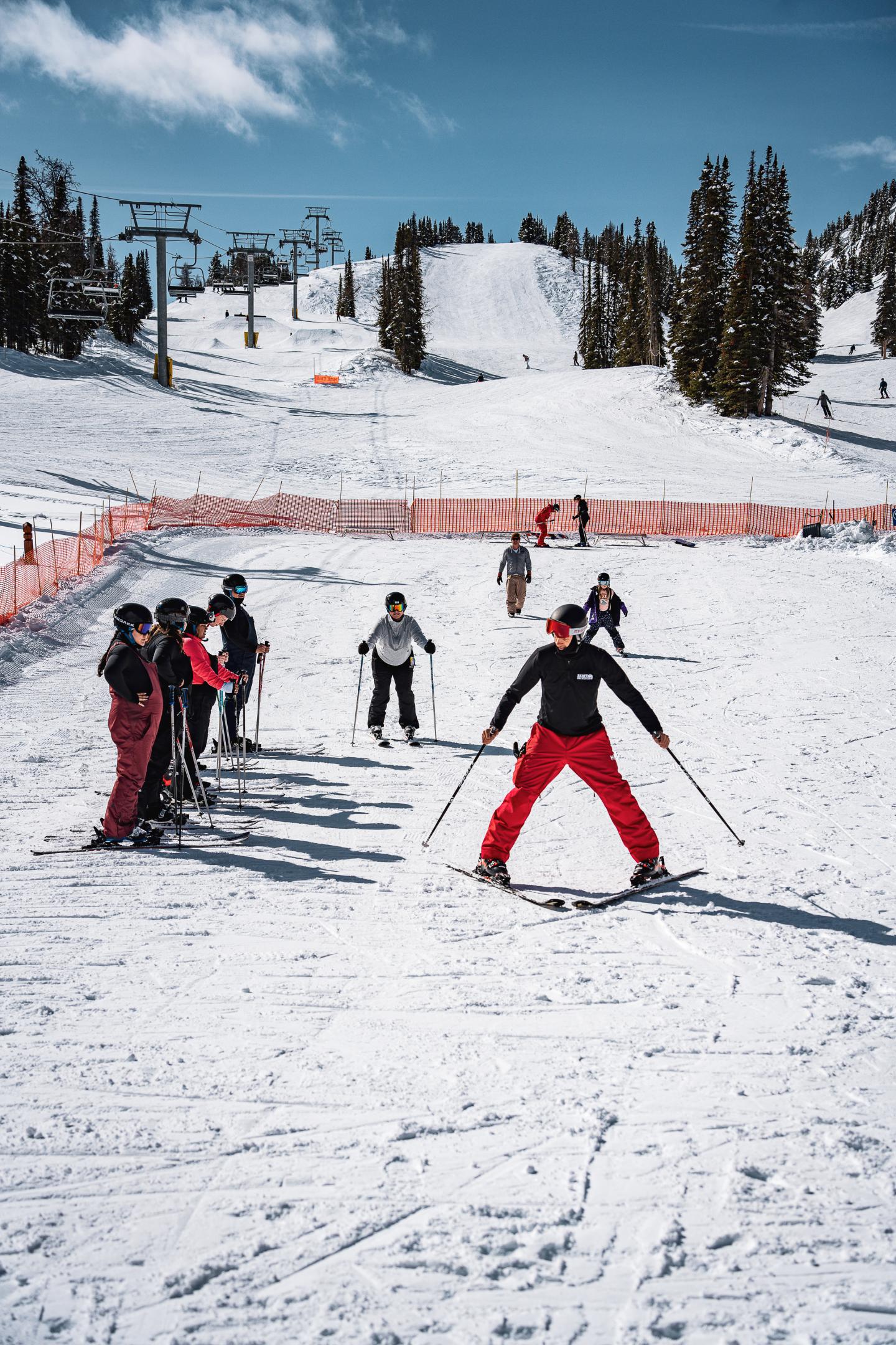 Ski instructor teaching a group on a snowy slope, under a clear blue sky.