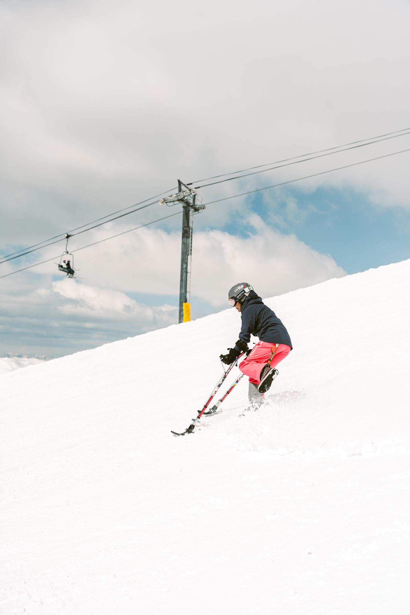 Skier in red pants carving down a snowy slope beneath a ski lift.