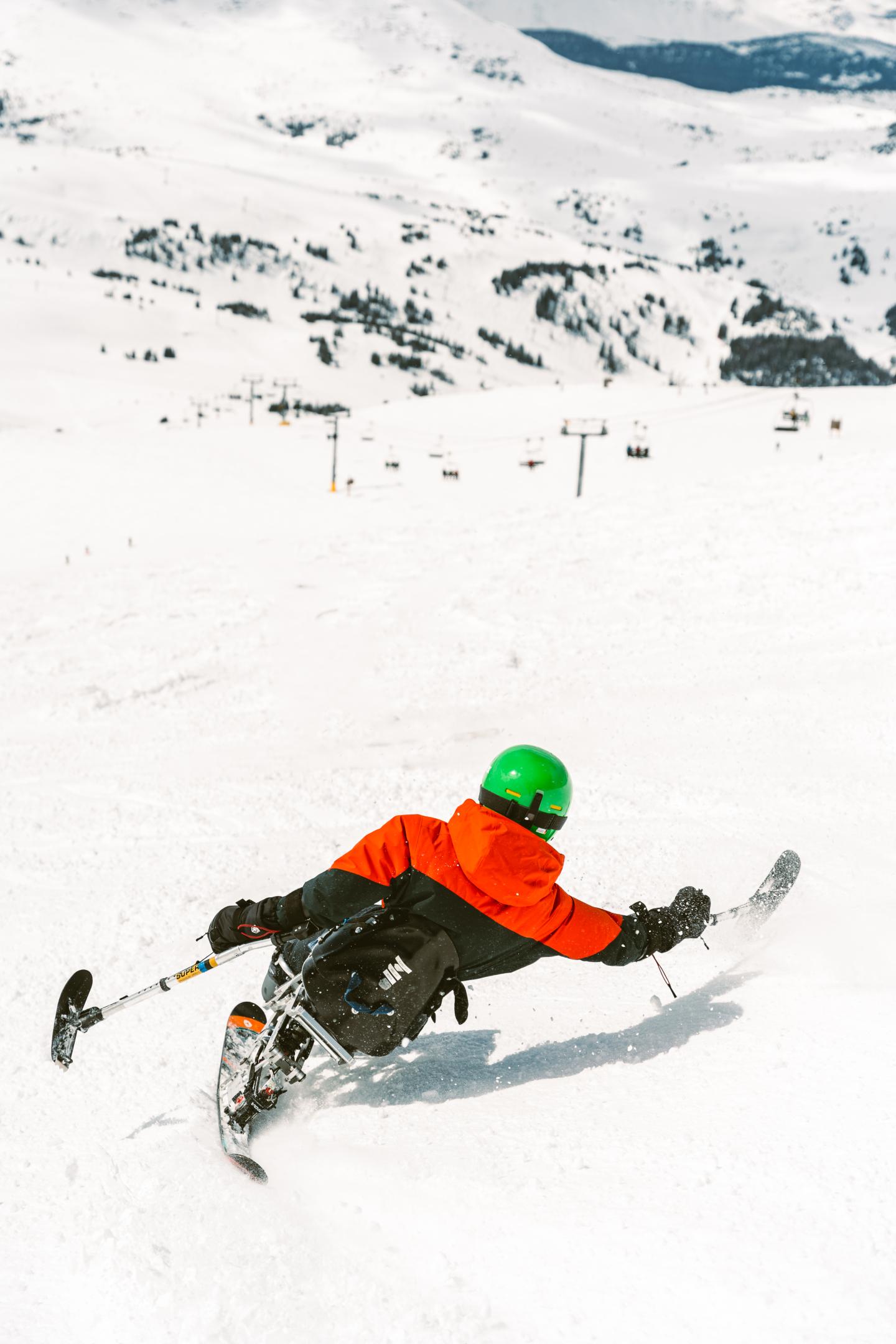 Skier in orange jacket carving through snowy mountain slope.