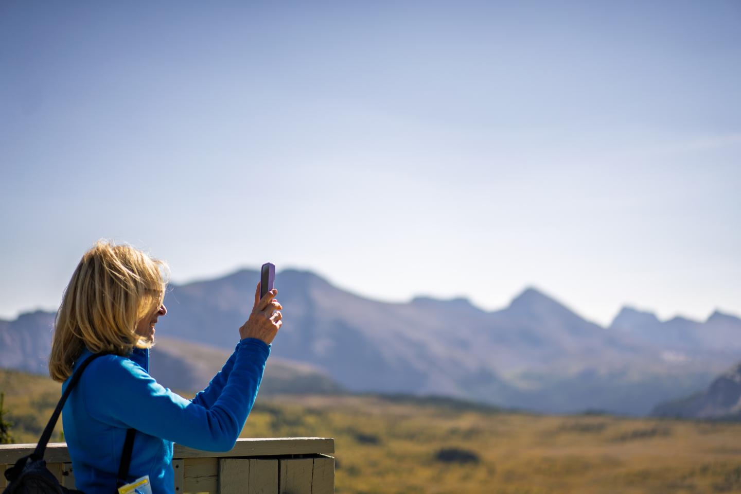 Woman in blue jacket taking a photo of mountains.