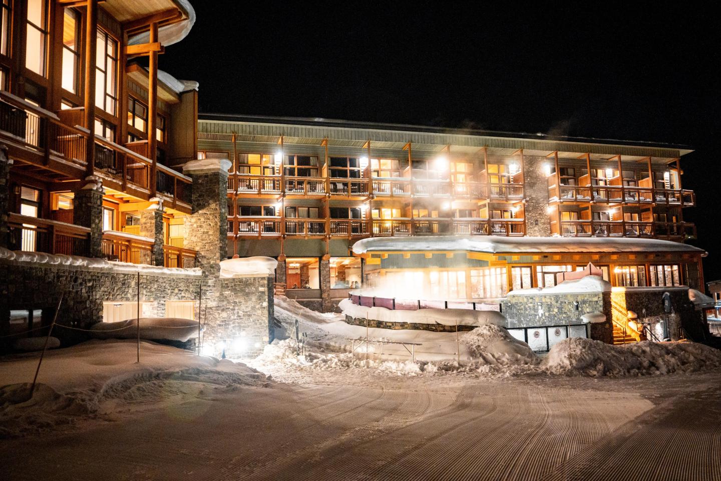 Nighttime view of a snowy, warmly lit mountain lodge complex.