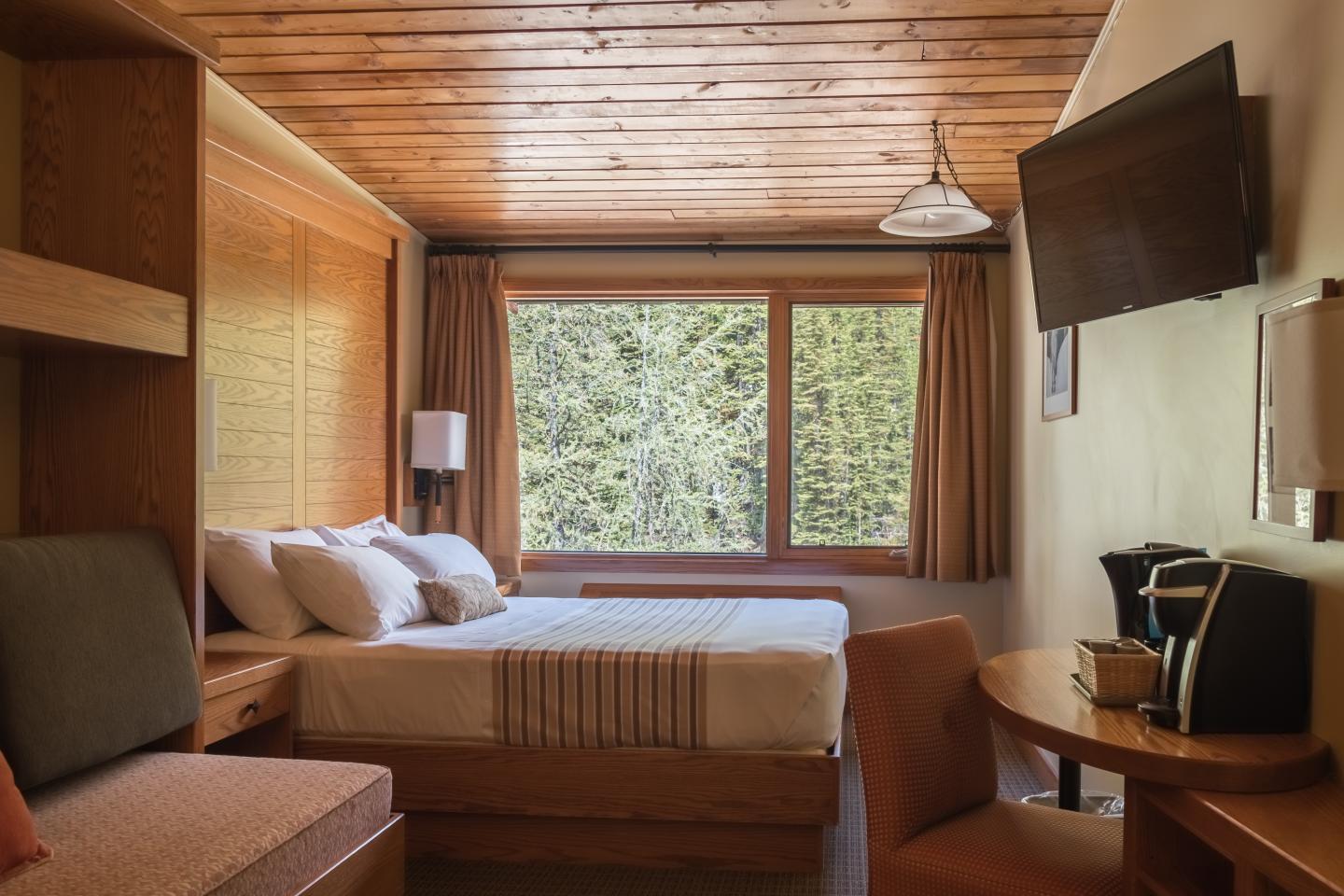 Cozy hotel room with a large window, bed, TV, and seating area.