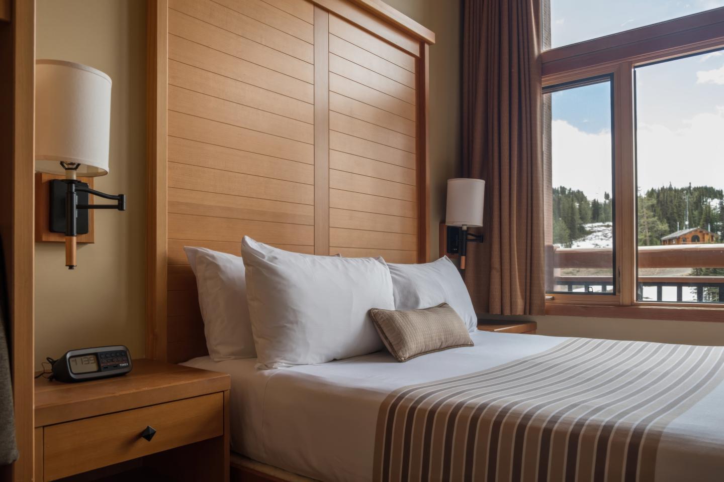 Cozy hotel bedroom with striped bedspread, wood paneling, and balcony view.