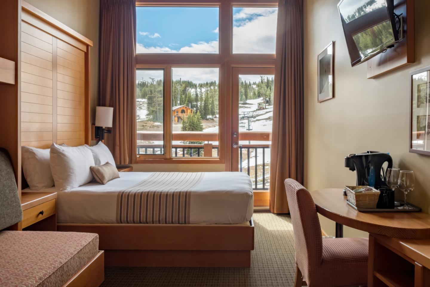 Cozy hotel room with twin beds, desk, and balcony view of mountains.