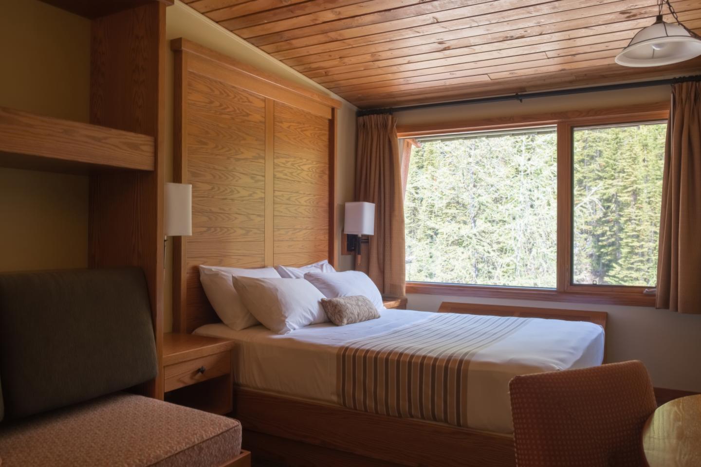 Cozy bedroom with wood accents, large window, and a neatly made bed.