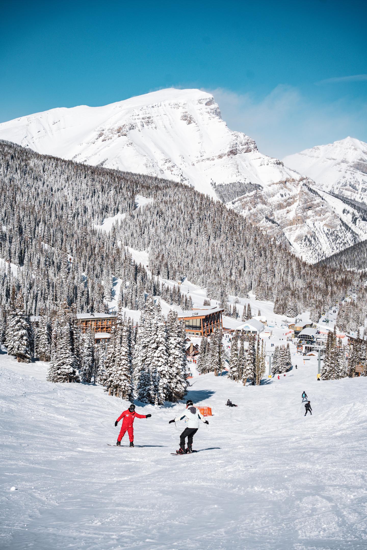Snowy mountain landscape with skiers, clear blue sky, and snow-covered trees.