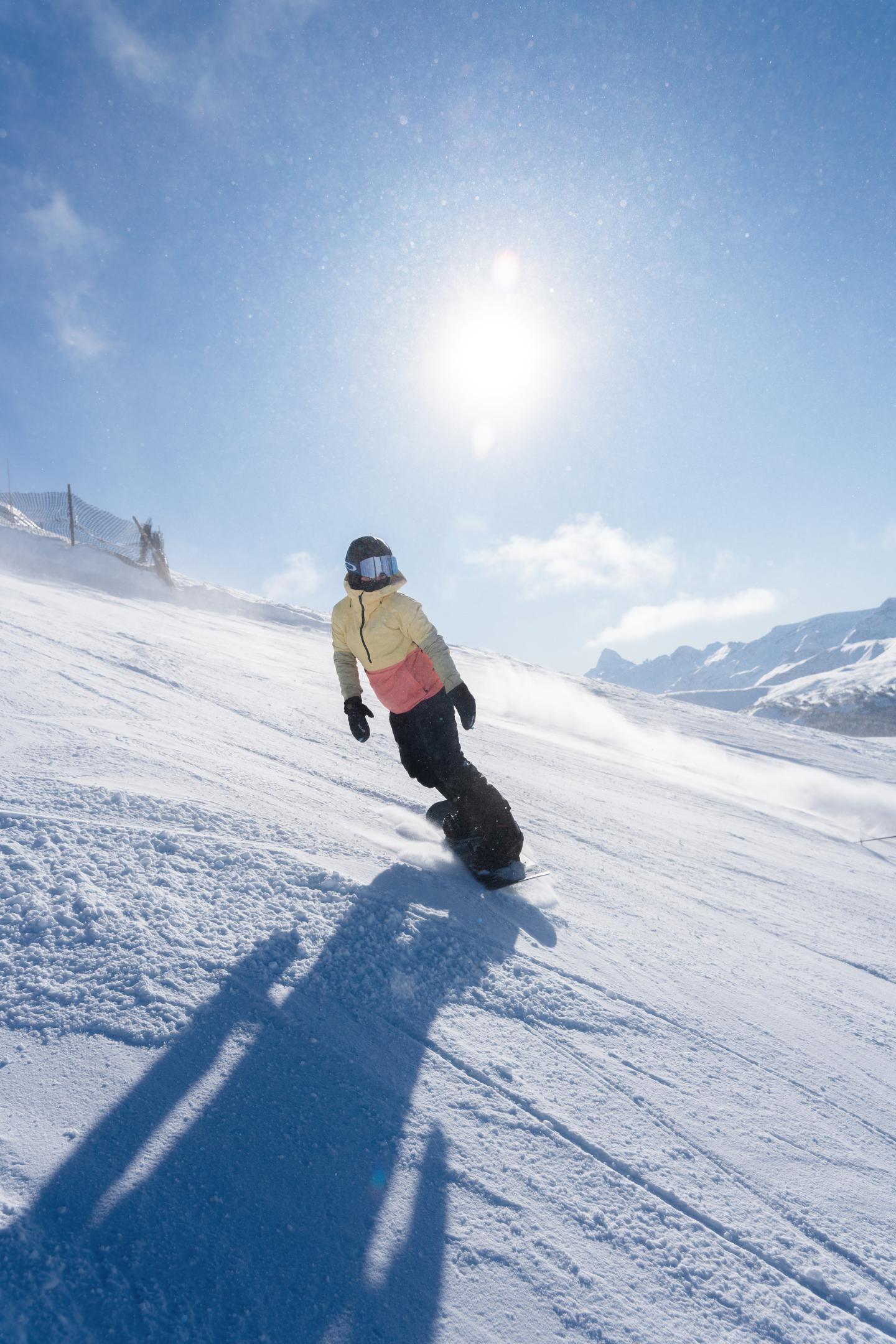 Snowboarder on a sunny, snowy slope with mountains in the background.