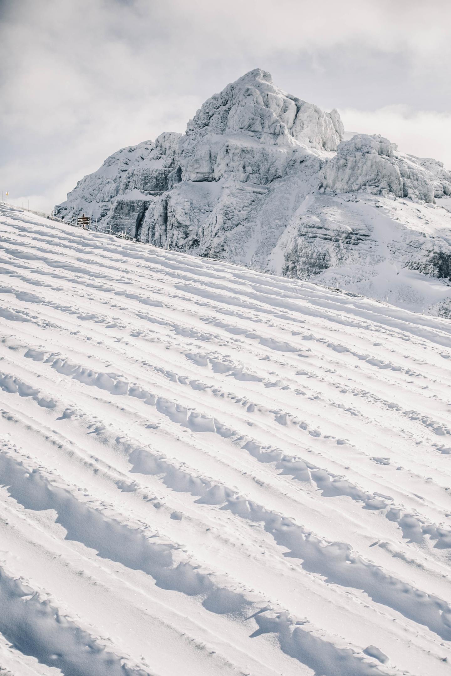 Snow-covered mountain with ridged foreground and cloudy sky.