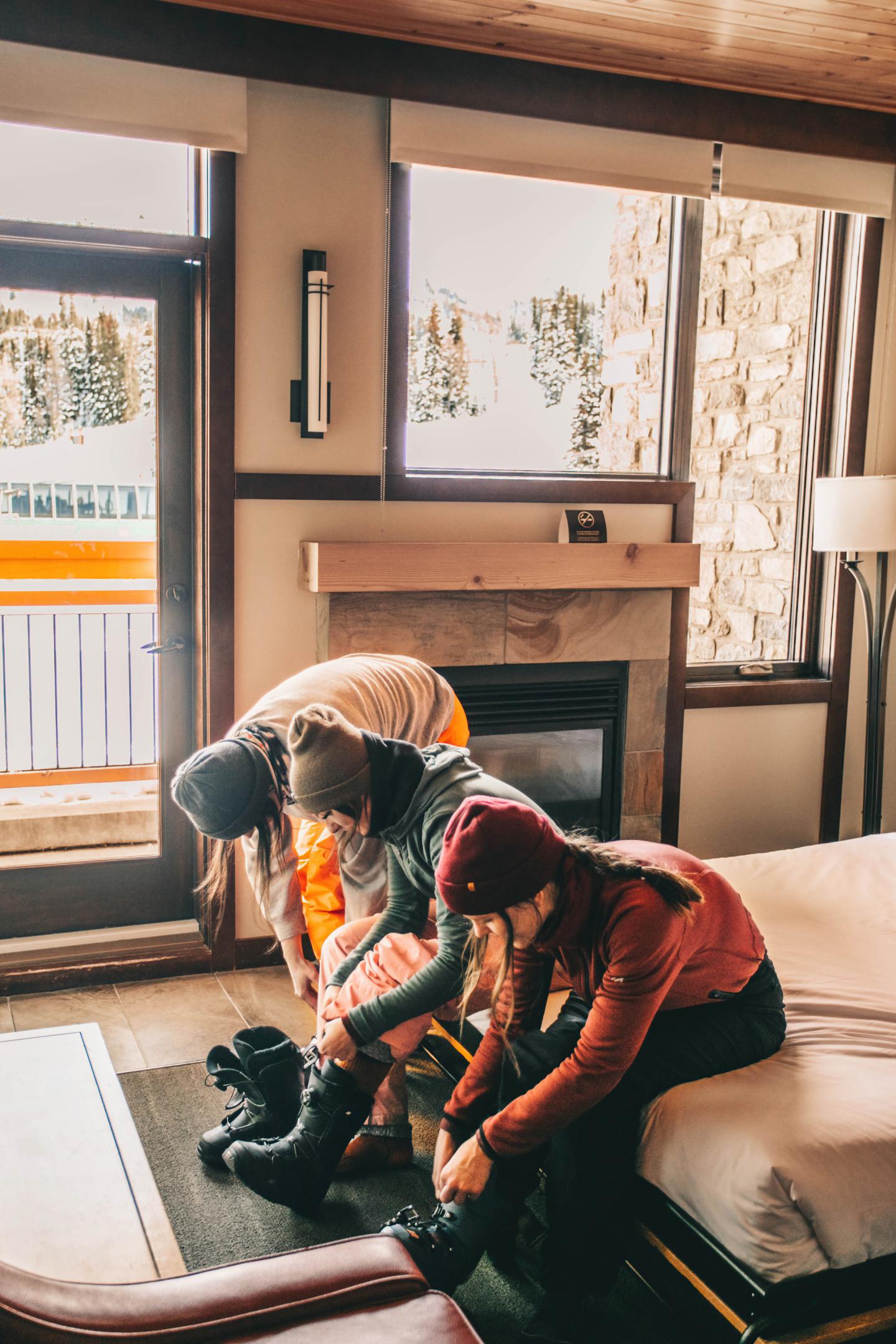 Two people in winter clothes putting on boots inside a cozy room.