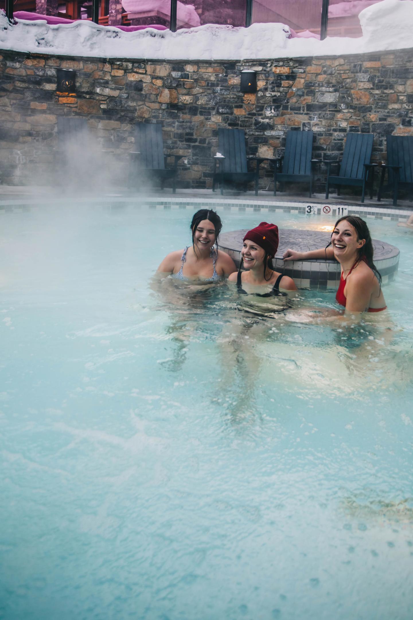 Three people in a steaming outdoor pool, smiling and relaxed.