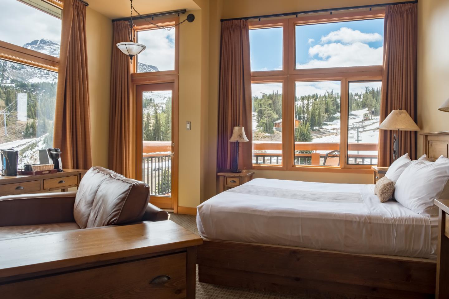 Sunlit bedroom with wooden furnishings, large windows, and mountain views.