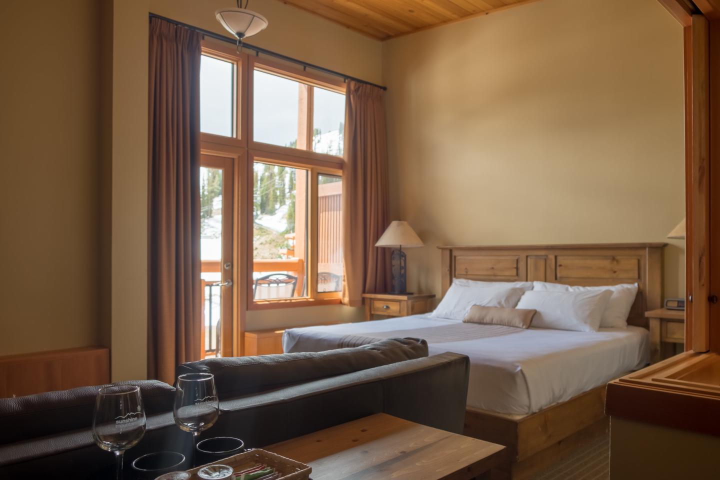 Warm wood-paneled bedroom with a large bed, window, and black leather sofa.