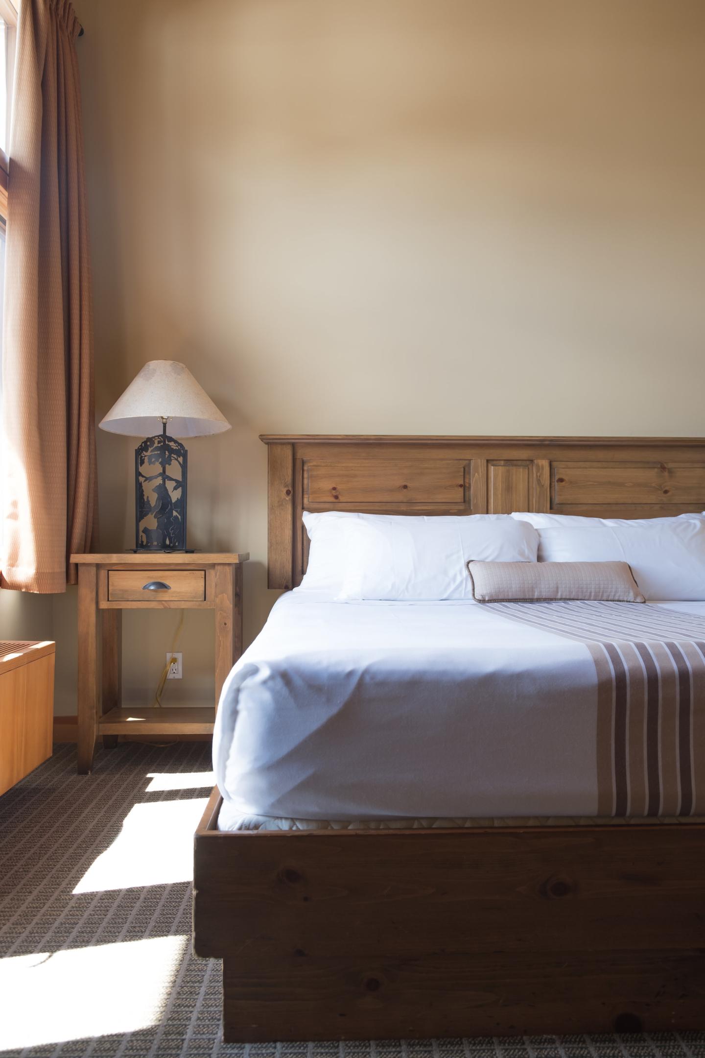 Sunlit rustic bedroom with a wooden bed, white linens, and striped throw.