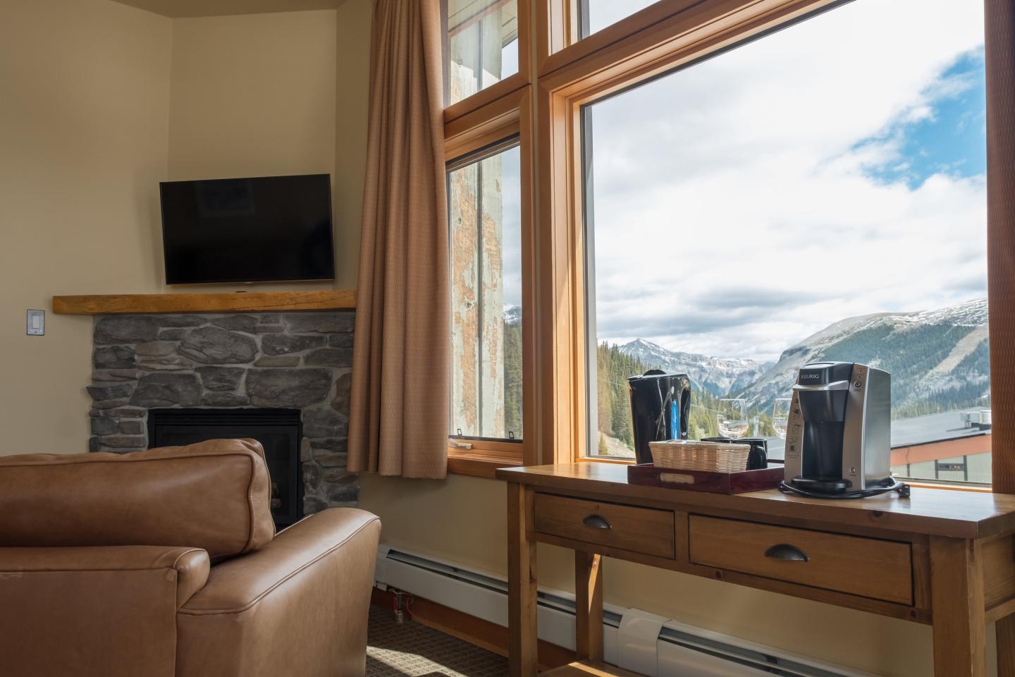 Cozy living room with leather sofa, stone fireplace, and mountain-view windows.