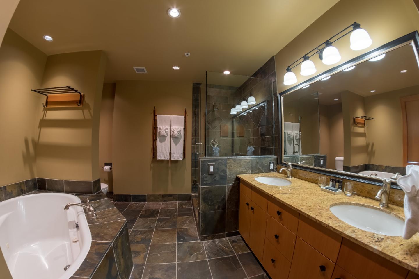 Spacious bathroom with double vanity, large mirror, tiled floor, and soaking tub.