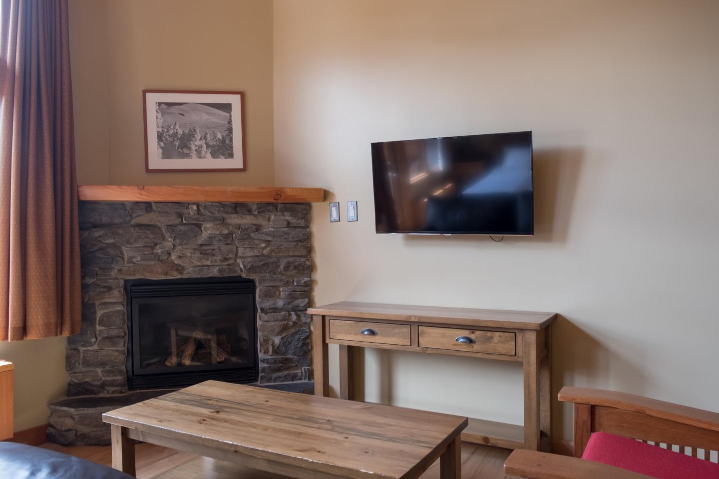 Cozy living room with stone fireplace, wall-mounted TV, and wooden coffee table.