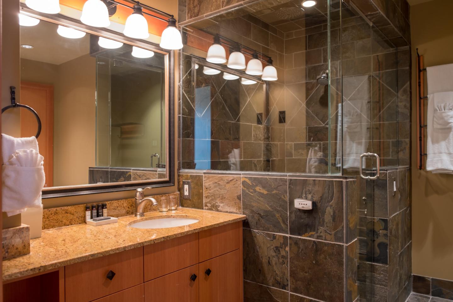 Warm bathroom with double vanity, large mirror, and glass-tiled shower.