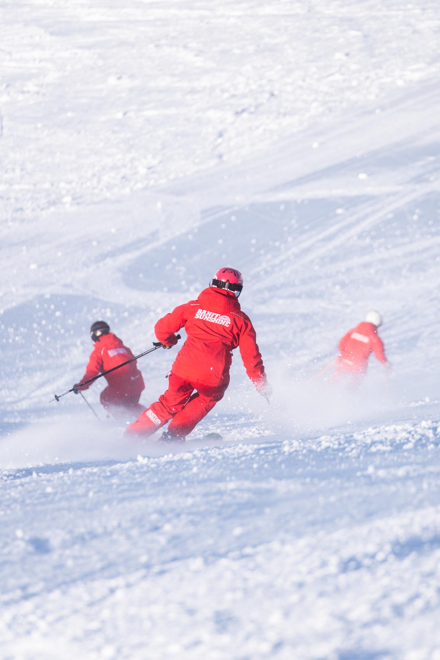 Skiers in red suits descending a snowy slope.