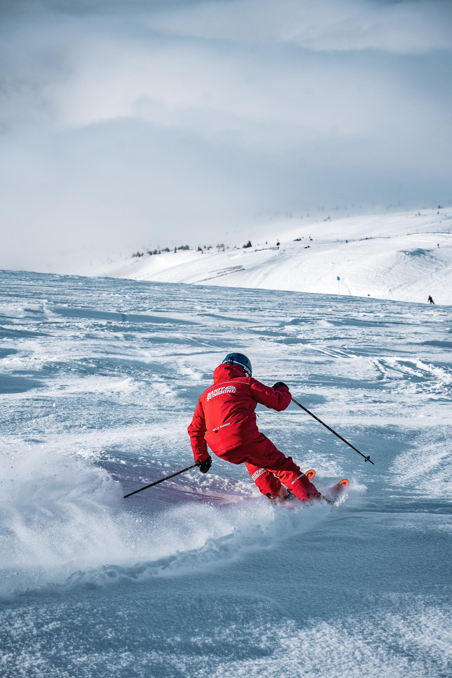 Skier in red navigating snowy slope under cloudy sky.