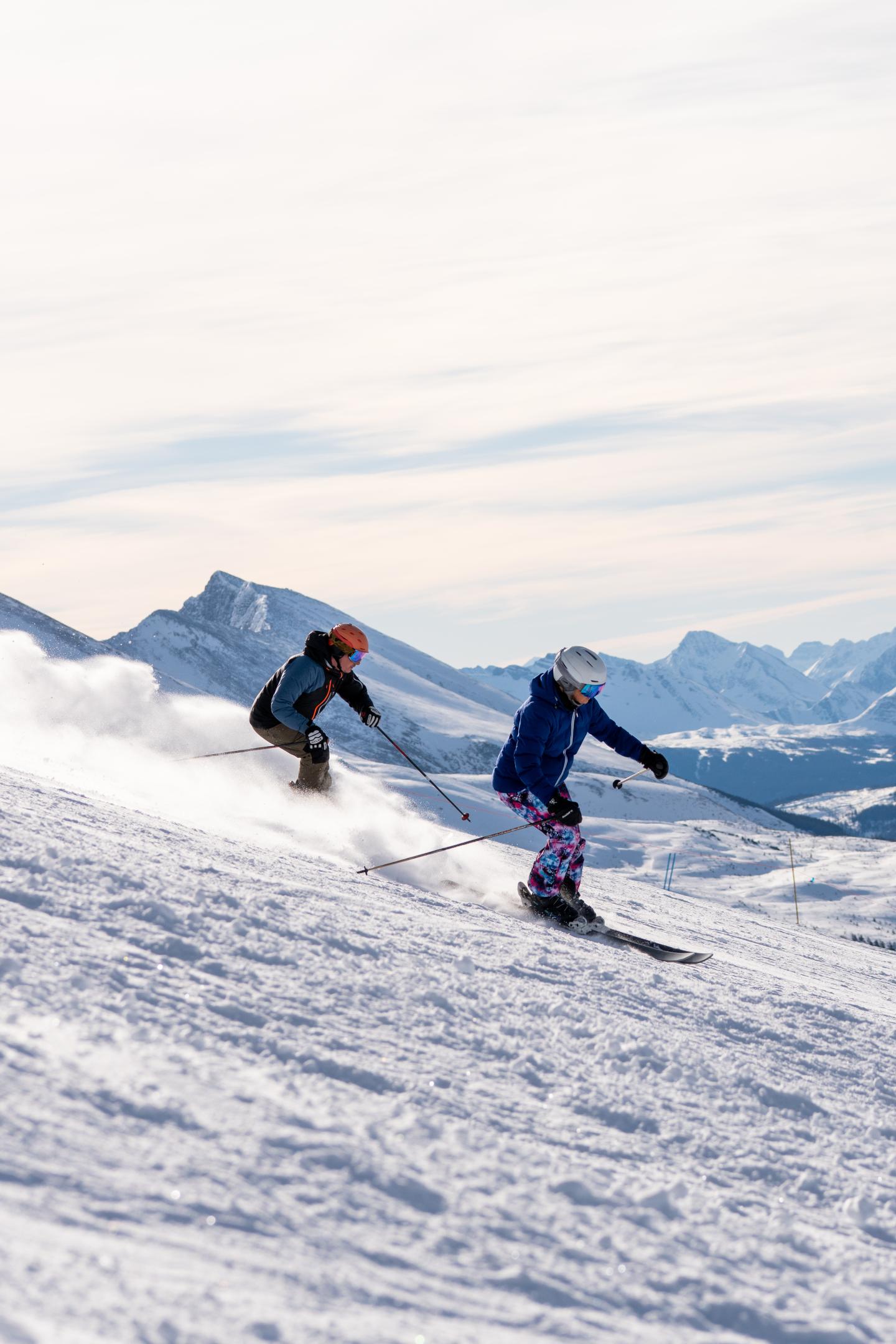 Two skiers on a snowy mountain slope under a clear sky.