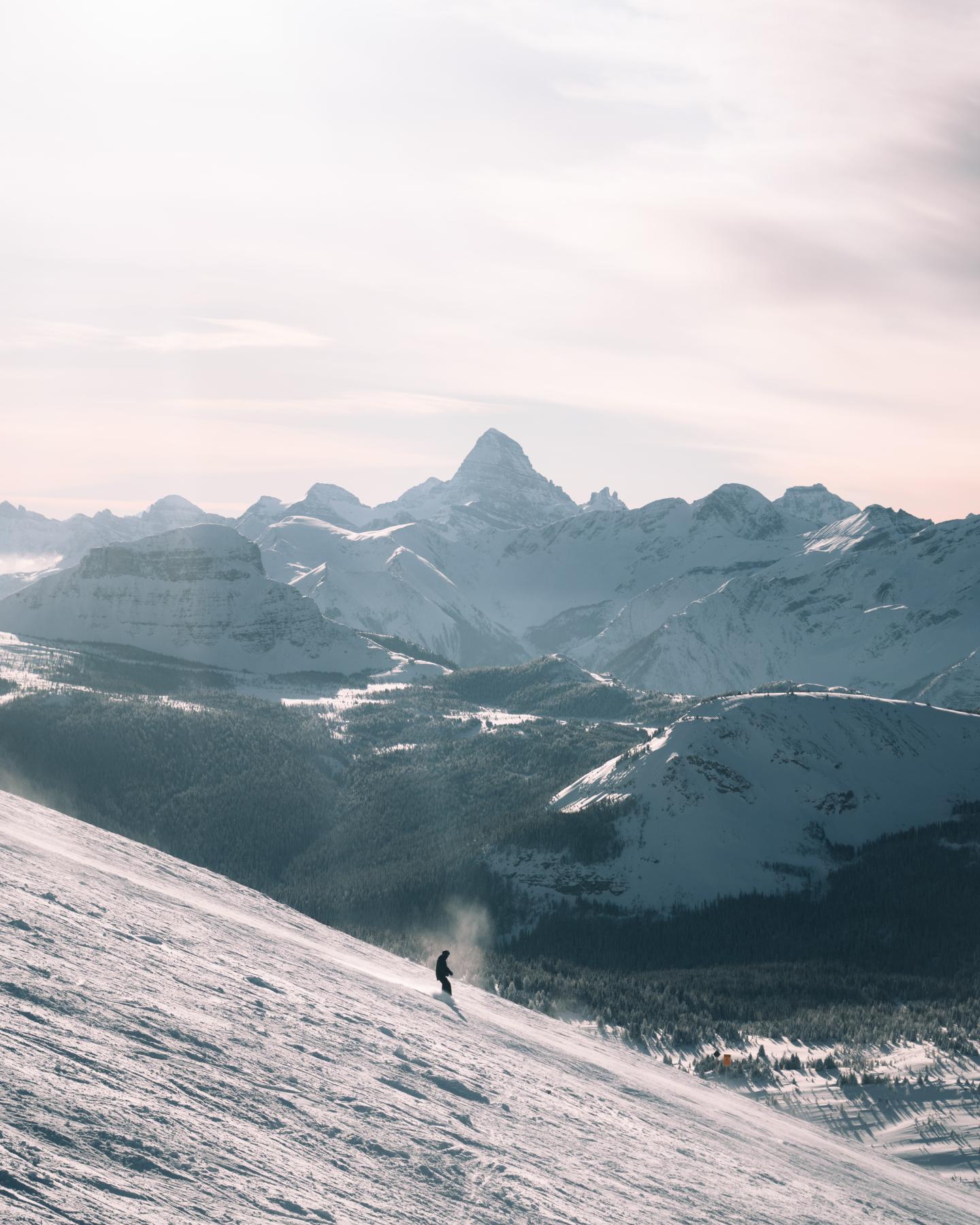 Lone skier descends a snowy mountain slope beneath jagged peaks.