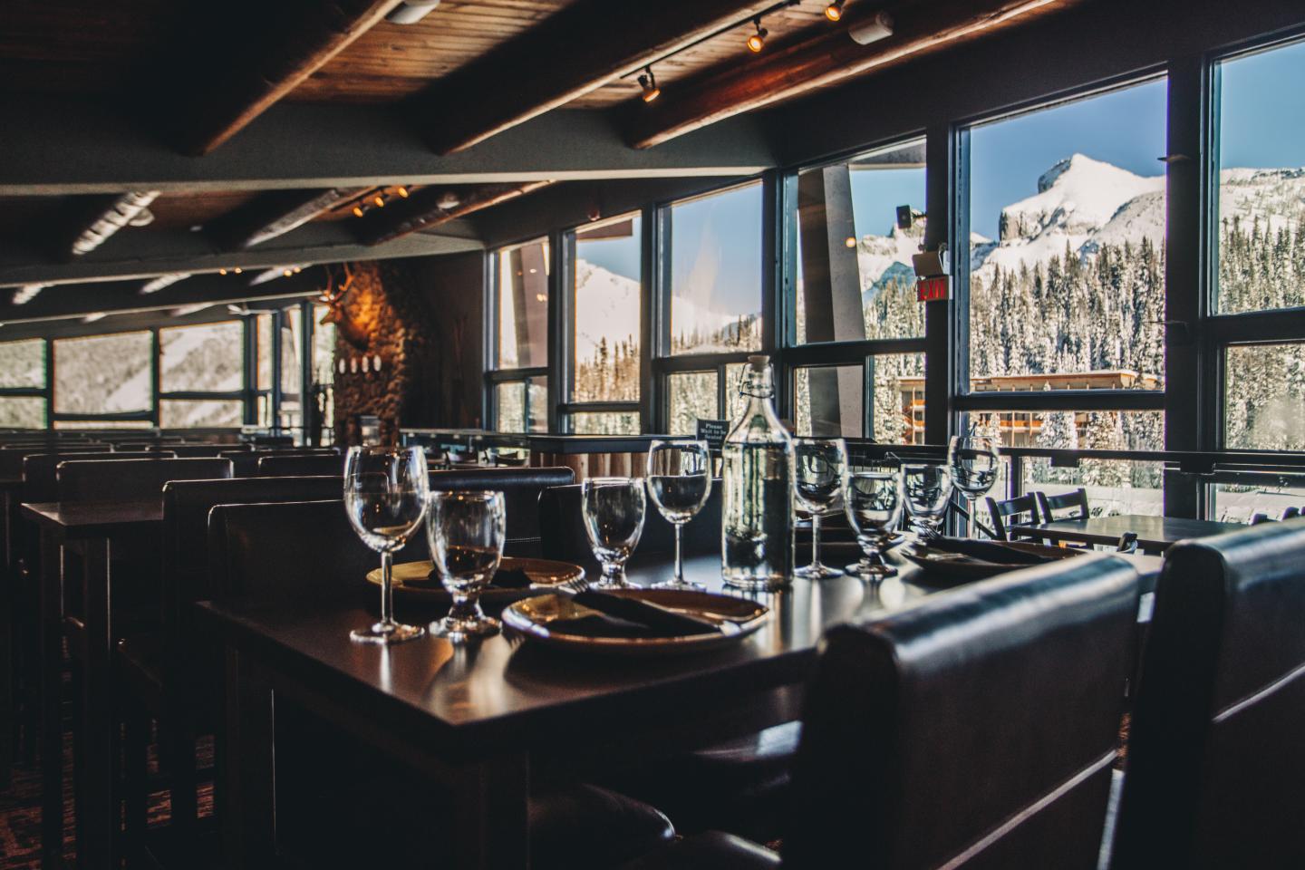 Upscale restaurant interior with set tables and mountain views through large windows.