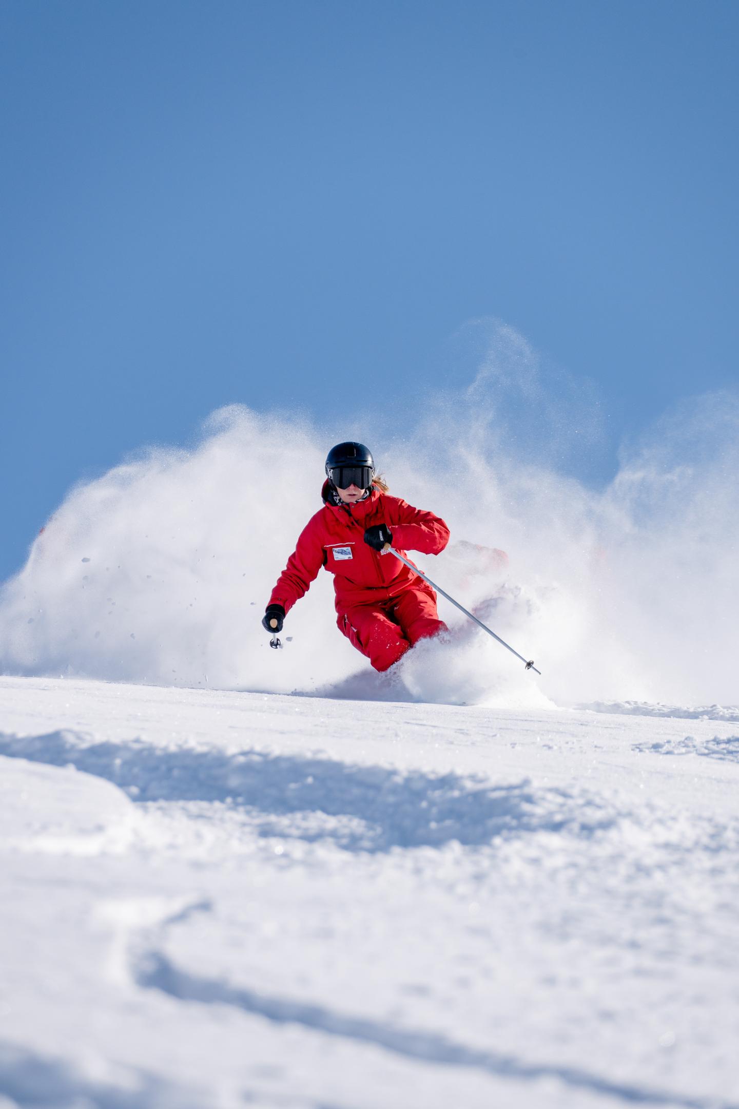 Skier in red gear descending snowy slope under clear blue sky.