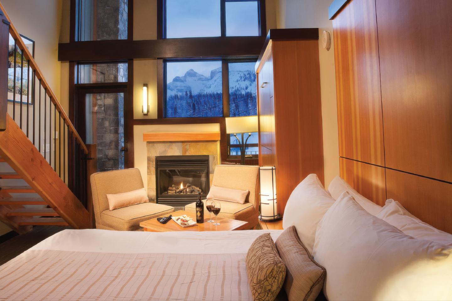 Cozy modern loft bedroom with fireplace, staircase, and mountain view.